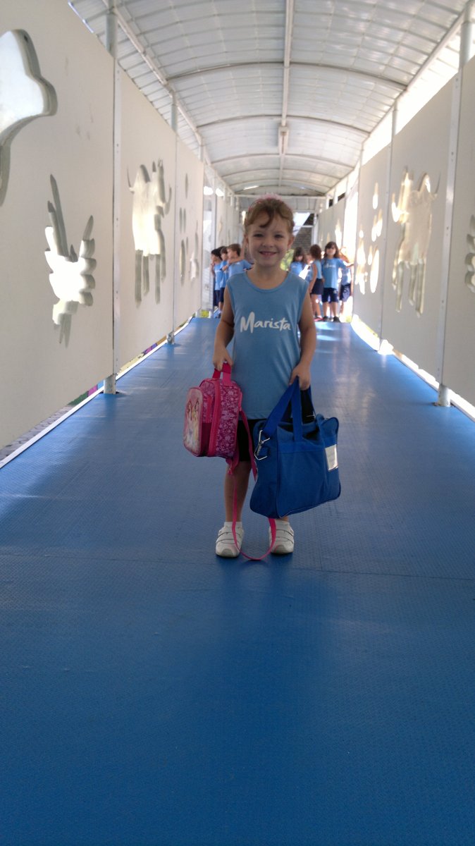 Livia, criança com diabetes tipo 1, de uniforme, andando pelo corredor da escola com as bolsas