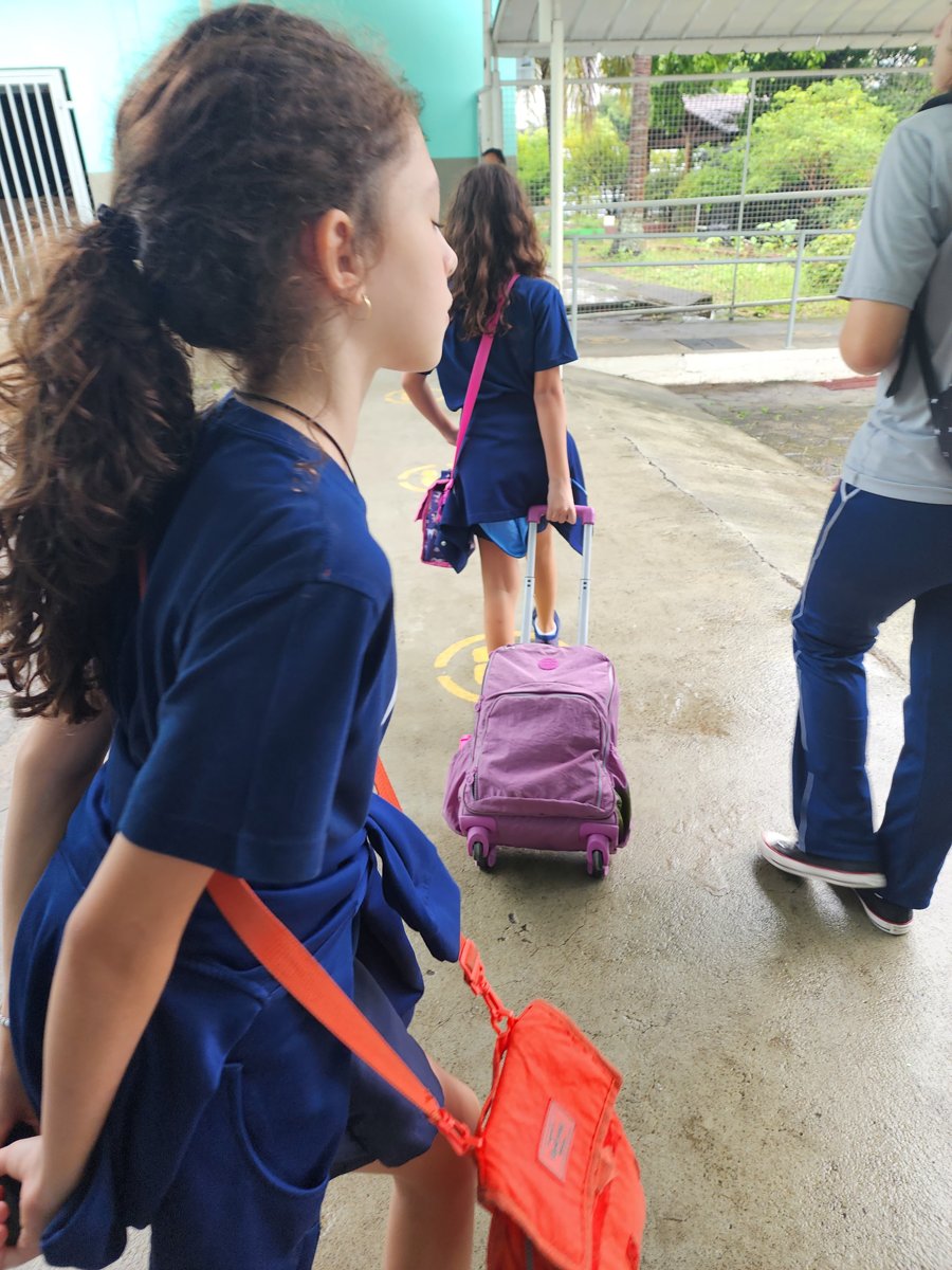 Livia, adolescente com diabetes tipo 1, de costas, entrando na escola com a mochila de rodinha