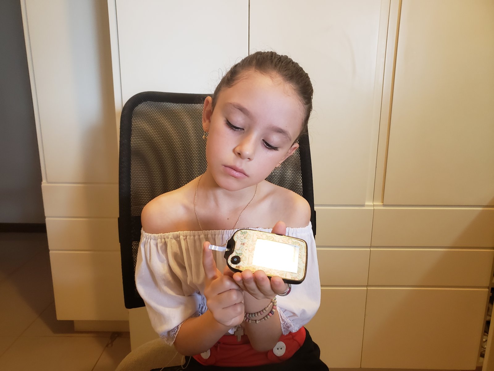 Livia, criança com diabetes tipo 1, sentada, olhando o resultado no medidor de glicose e cetona